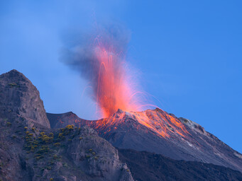 Een foto van een vulkaanuitbarsting. Er spat rode lava uit de volkaan de lucht in.