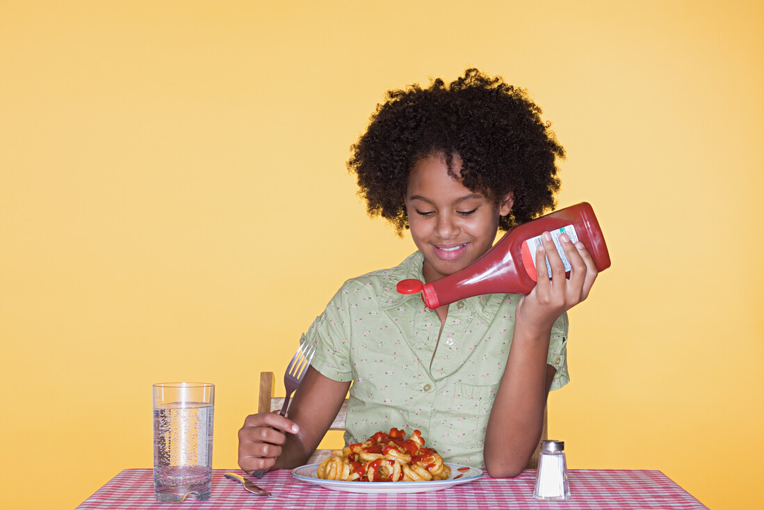 Een foto van een meisje die een bot patat eet met ketchup en zout.